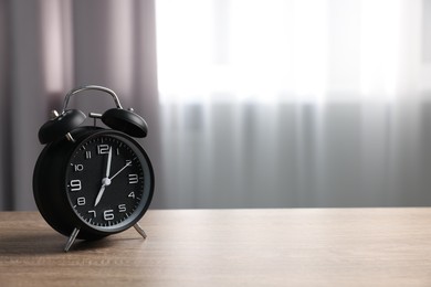 Photo of Black alarm clock on wooden table indoors, space for text