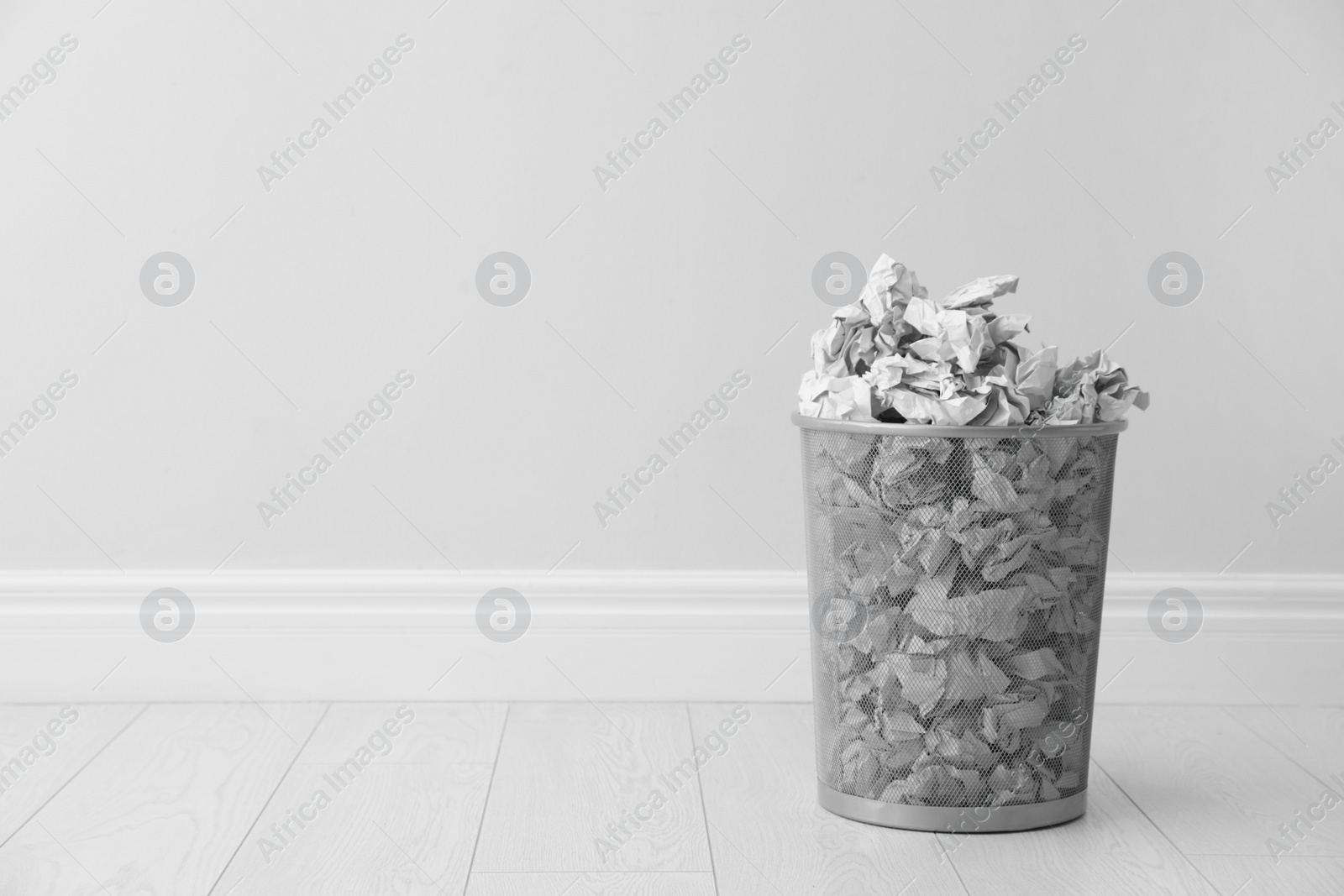 Photo of Metal bin and crumpled paper against light wall, space for text