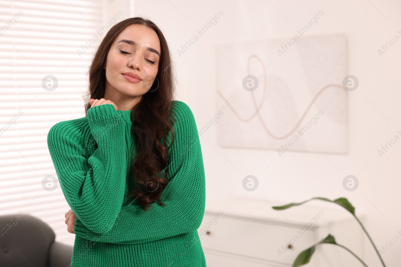 Photo of Beautiful young woman in stylish warm sweater at home, space for text