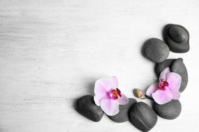 Stones with orchid flowers and space for text on white wooden background, flat lay. Zen lifestyle