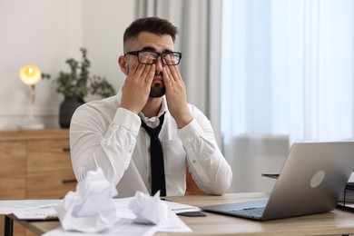 Photo of Overwhelmed man sitting at table with laptop and documents in office