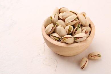 Photo of Delicious pistachios in bowl on white textured table. Space for text