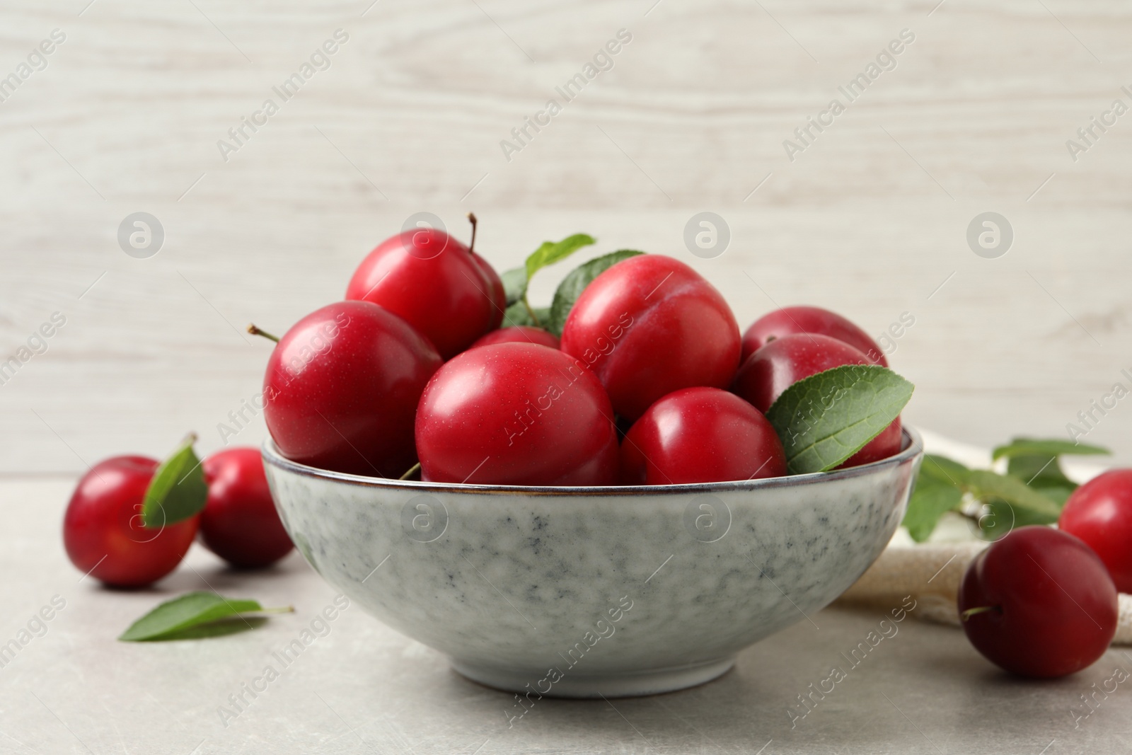 Photo of Delicious ripe cherry plums with leaves on light table