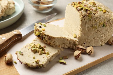 Photo of Tasty halva with pistachios and knife on grey table, closeup