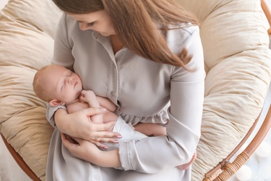 Young mother with her newborn baby in papasan chair at home