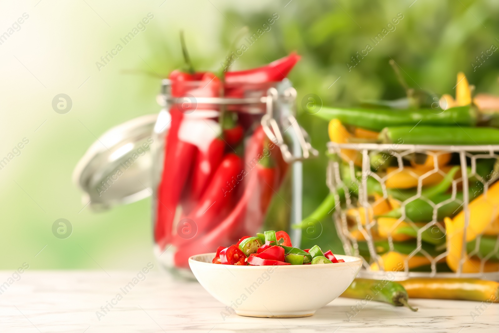 Photo of Bowl with cut chili peppers on table against blurred background