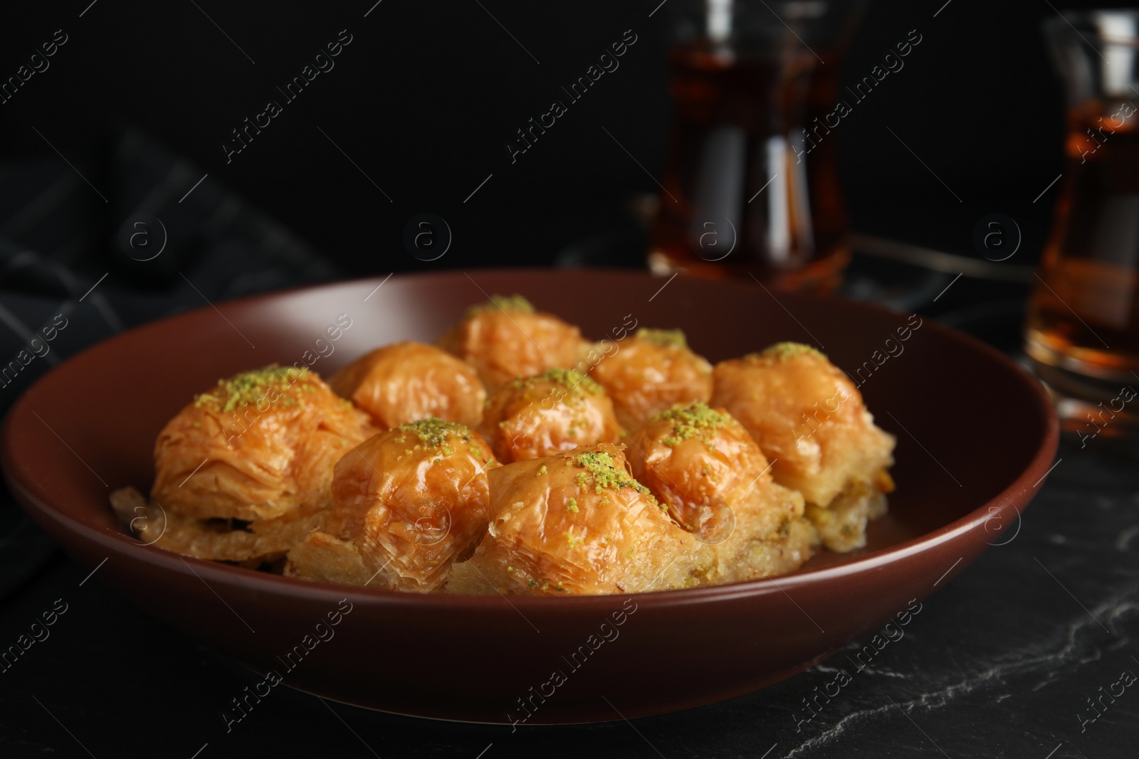 Photo of Delicious sweet baklava in bowl on black table, closeup