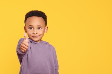 Photo of African-American boy showing thumb up on yellow background. Space for text