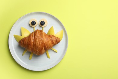 Funny crab made with croissant, fruits and berries on yellowish green background, top view. Space for text