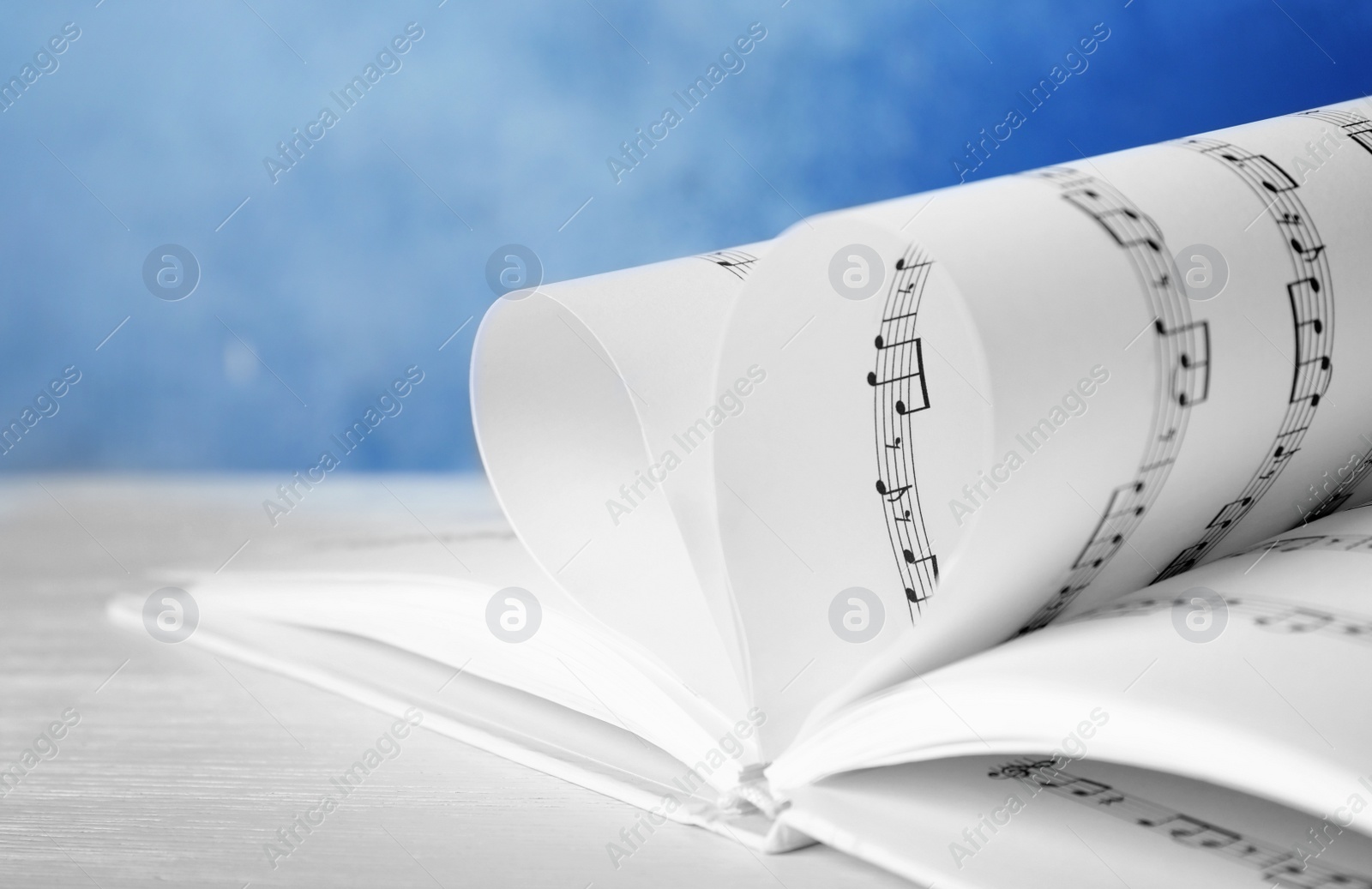 Photo of Heart made of book pages with music notes on table against color background, closeup. Space for text