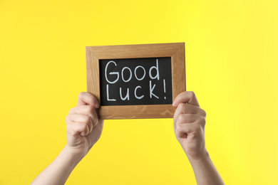 Woman holding blackboard with words GOOD LUCK on yellow background, closeup