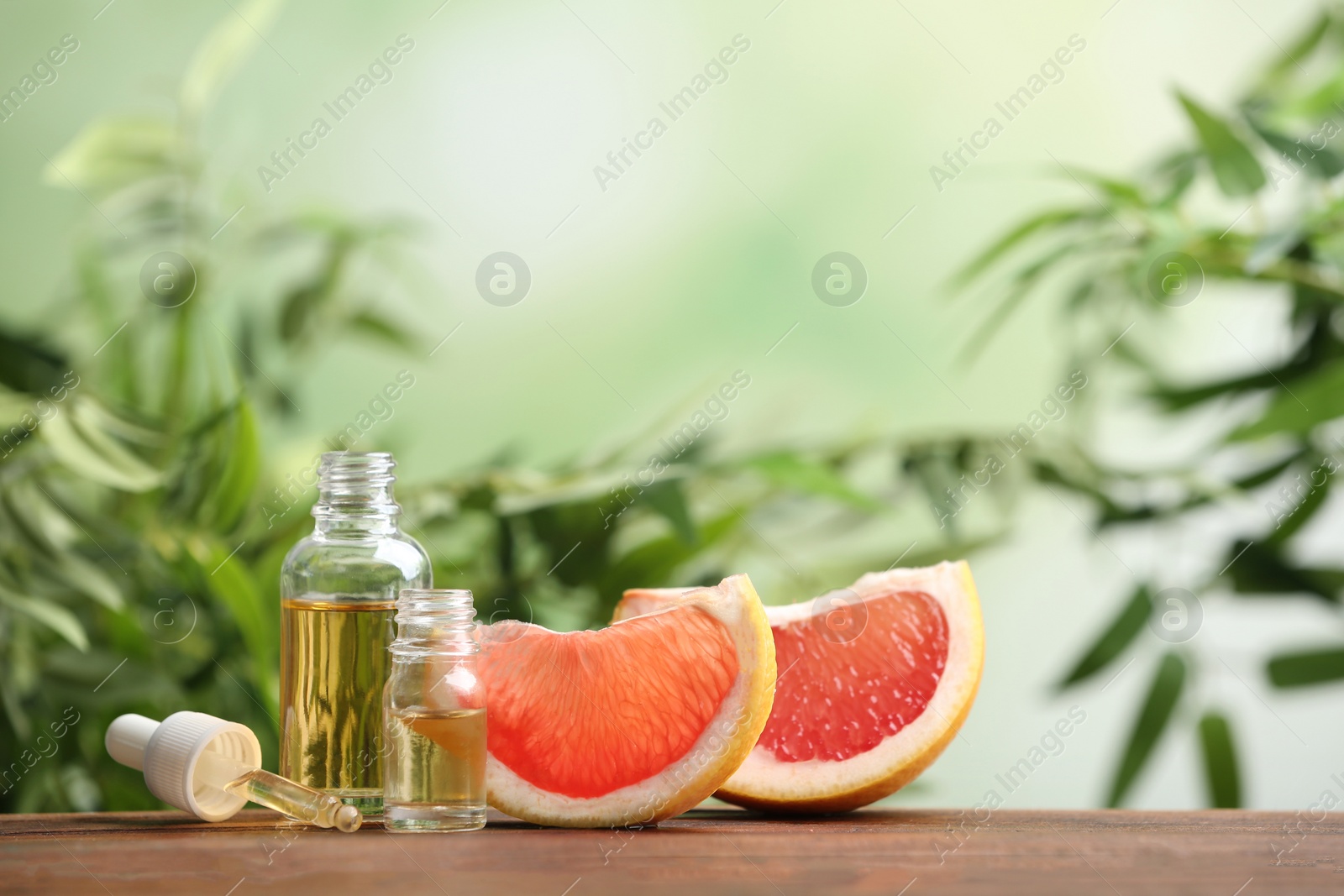 Photo of Bottles of essential oil and grapefruit slices on table against blurred background. Space for text