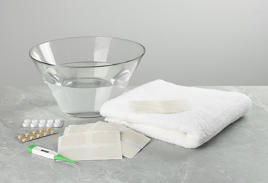 Photo of Mustard plasters, pills, thermometer, towel and bowl of water on light grey marble table