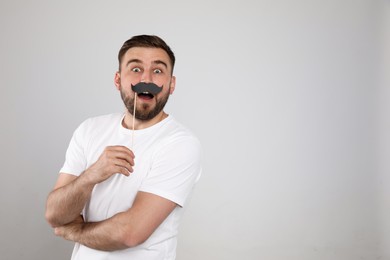 Emotional man with fake mustache on light grey background, space for text