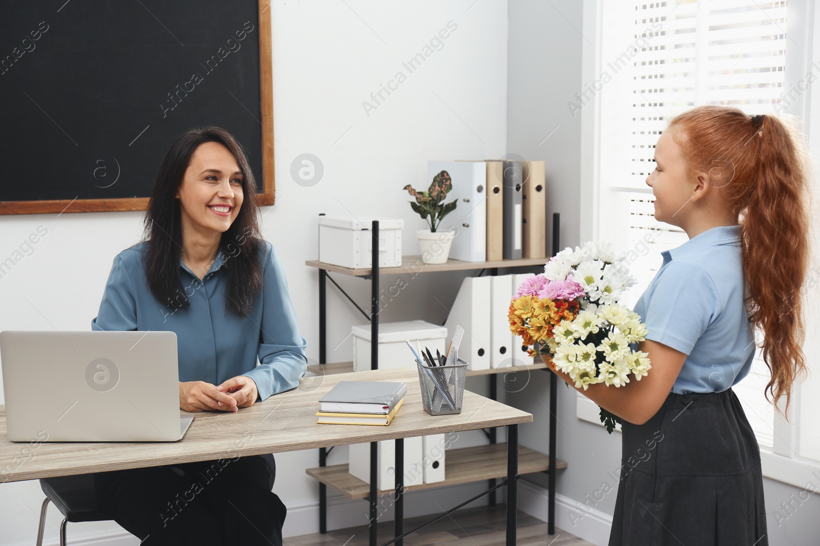 Photo of Schoolgirl with bouquet congratulating her pedagogue in classroom. Teacher's day