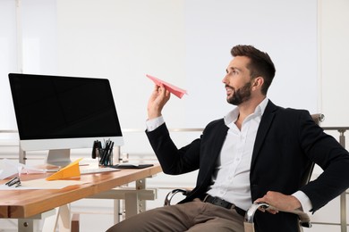 Handsome businessman playing with paper plane at desk in office