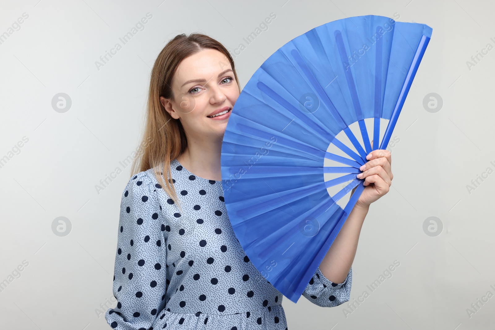 Photo of Happy woman with blue hand fan on light grey background