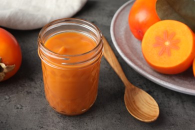 Photo of Delicious persimmon jam in glass jar served on gray table, closeup