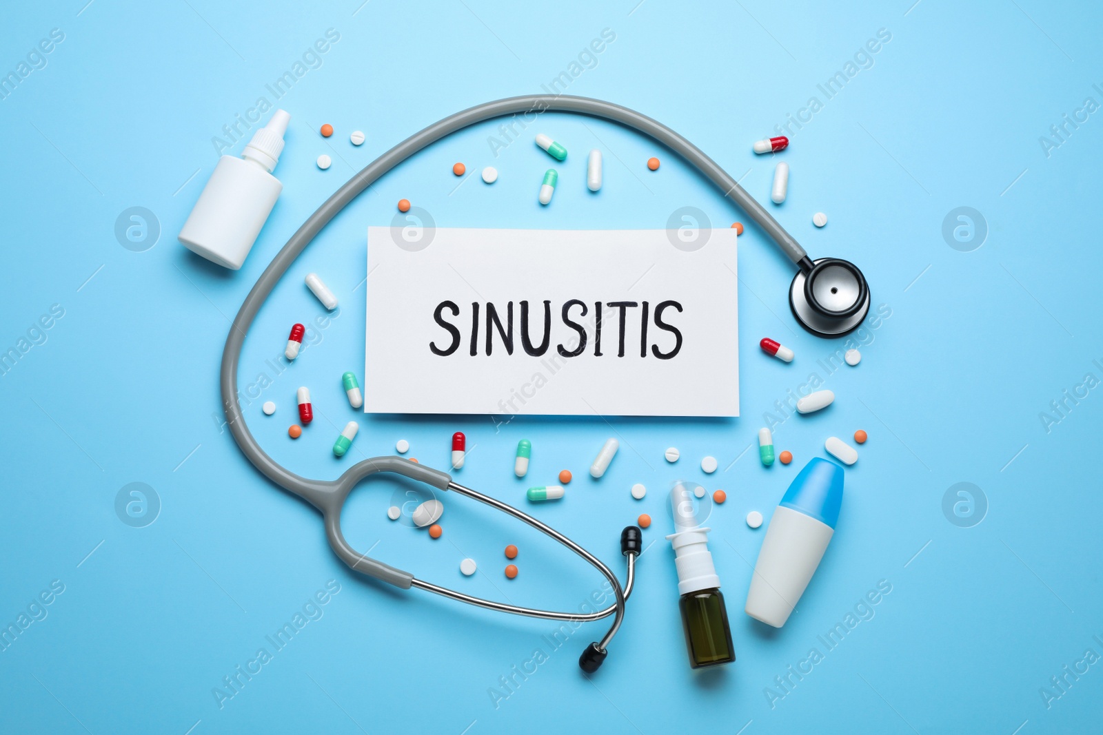 Photo of Card with word SINUSITIS, stethoscope and different drugs on light blue background, flat lay