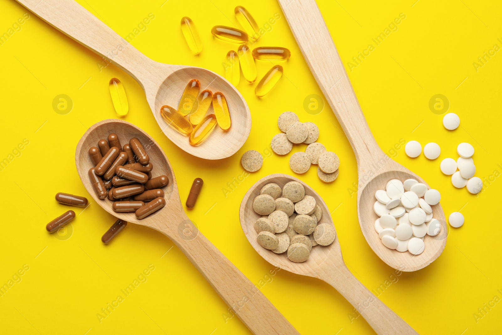 Photo of Wooden spoons and different dietary supplements on yellow background, flat lay