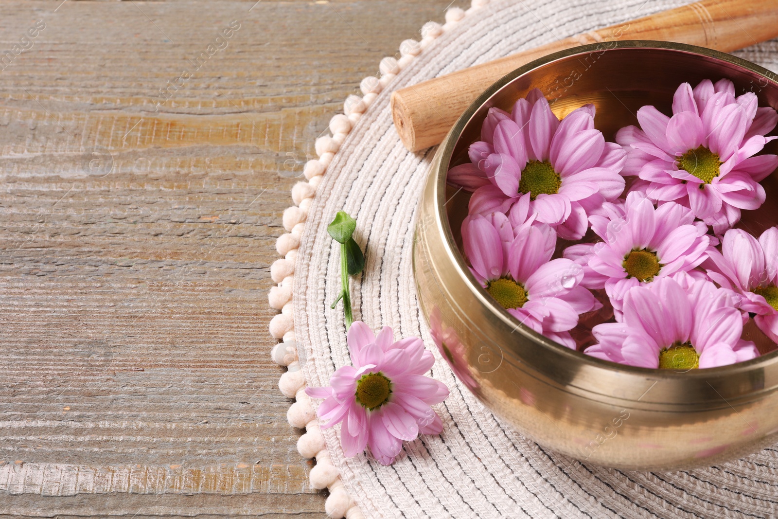 Photo of Tibetan singing bowl with water, beautiful flowers and mallet on wooden table, closeup. Space for text