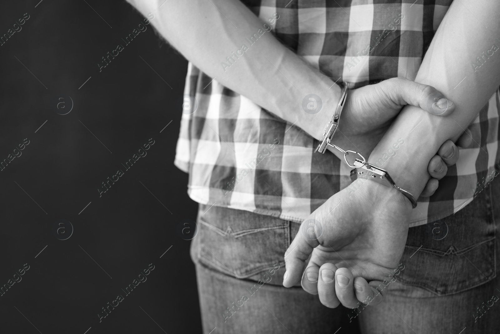Photo of Criminal detained in handcuffs against dark background, space for text. Black and white effect