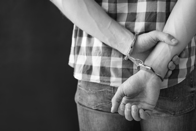 Photo of Criminal detained in handcuffs against dark background, space for text. Black and white effect