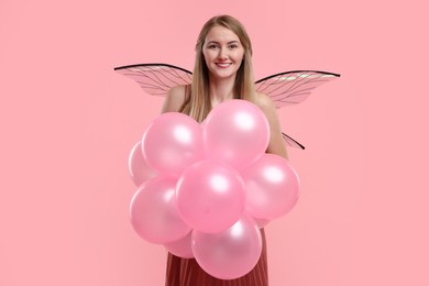 Beautiful girl in fairy costume with wings and balloons on pink background