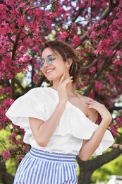 Photo of Attractive young woman posing near blossoming tree on sunny spring day