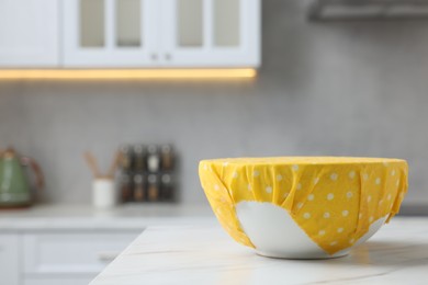 Photo of Bowl covered with beeswax food wrap on white table indoors, space for text