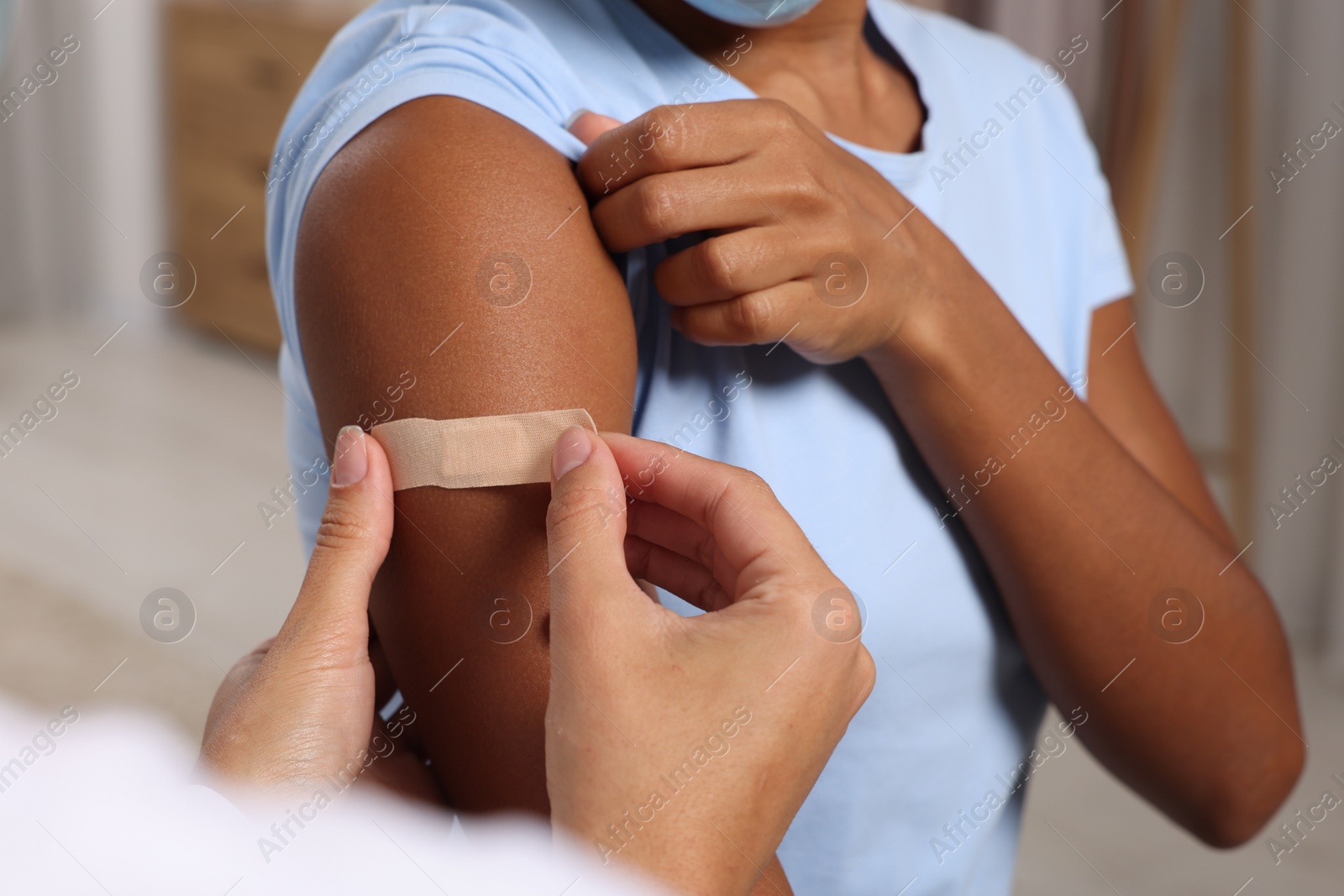 Photo of Doctor putting adhesive bandage on young woman's arm after vaccination indoors, closeup