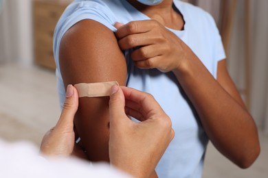 Doctor putting adhesive bandage on young woman's arm after vaccination indoors, closeup