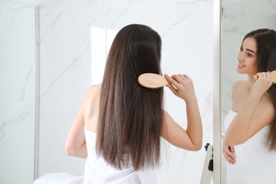 Photo of Beautiful young woman with hair brush looking into mirror in bathroom