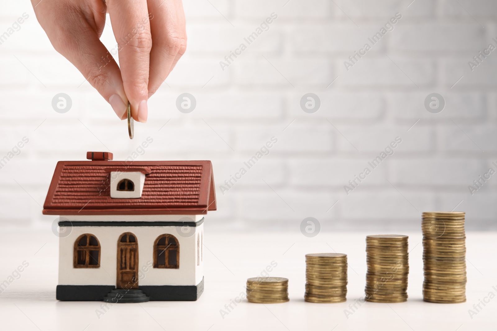 Photo of Woman putting coin into house model at light table with stacked coins, closeup