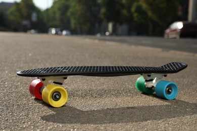 Black skateboard with colorful wheels on asphalt outdoors