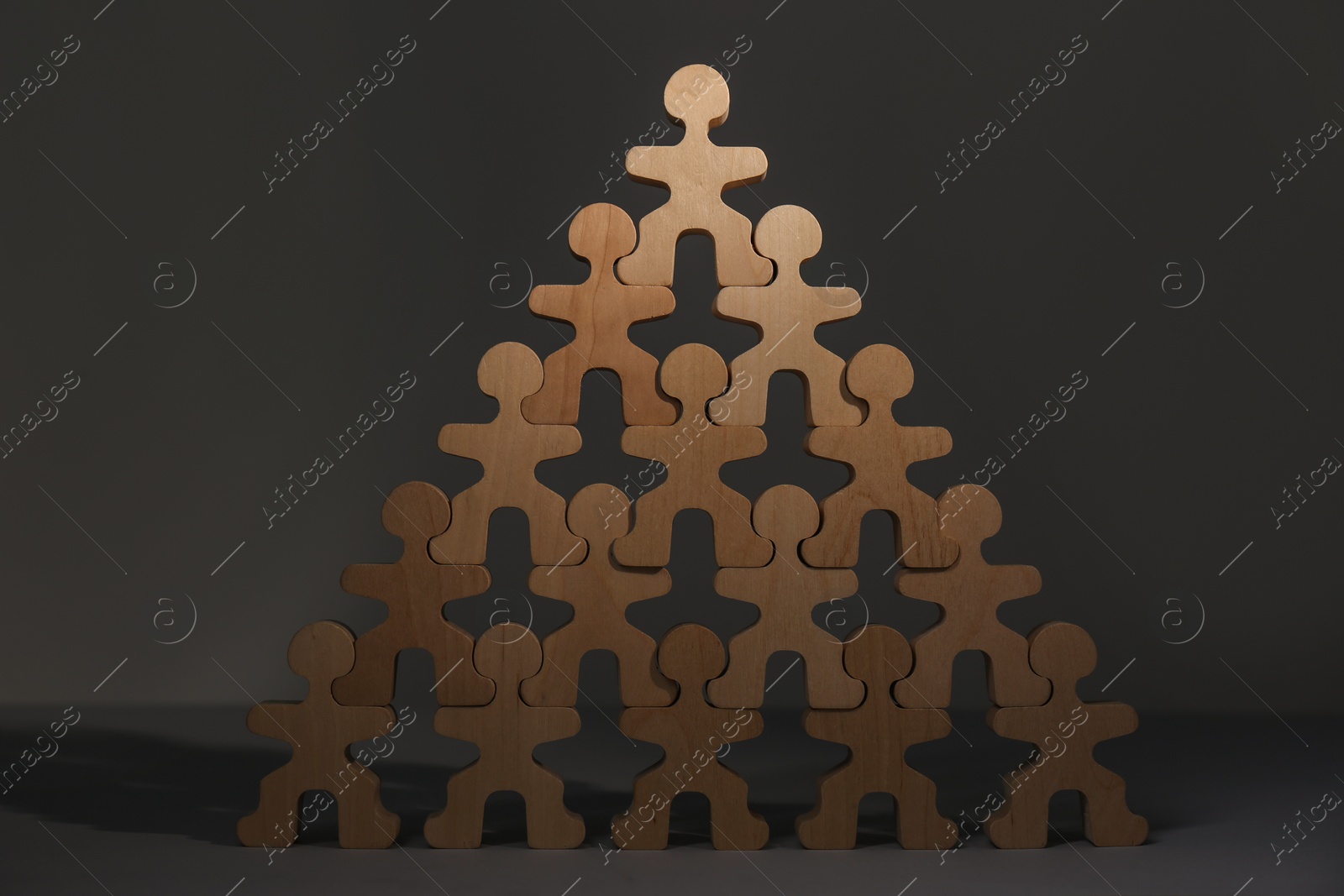 Photo of Recruitment process, job competition concept. Pyramid of wooden human figures with noticeable one on top as prime applicant on grey table