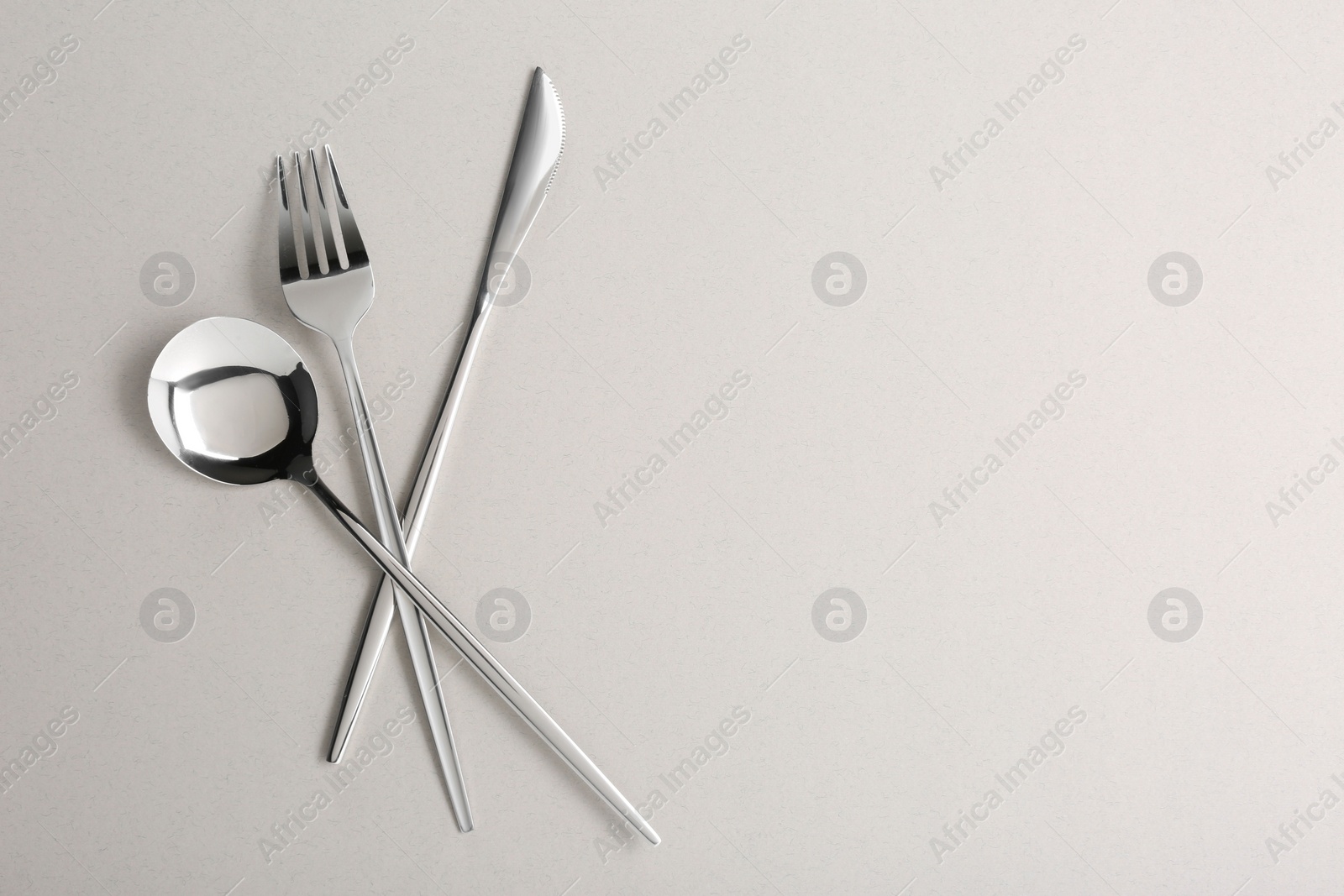 Photo of Spoon, fork and knife on light grey background, flat lay. Space for text