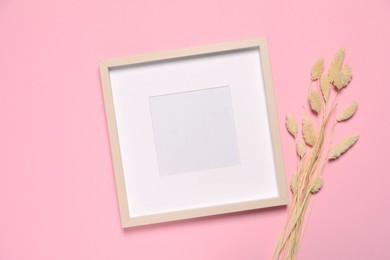 Photo of Empty photo frame and dry decorative spikes on pink background, flat lay. Space for design