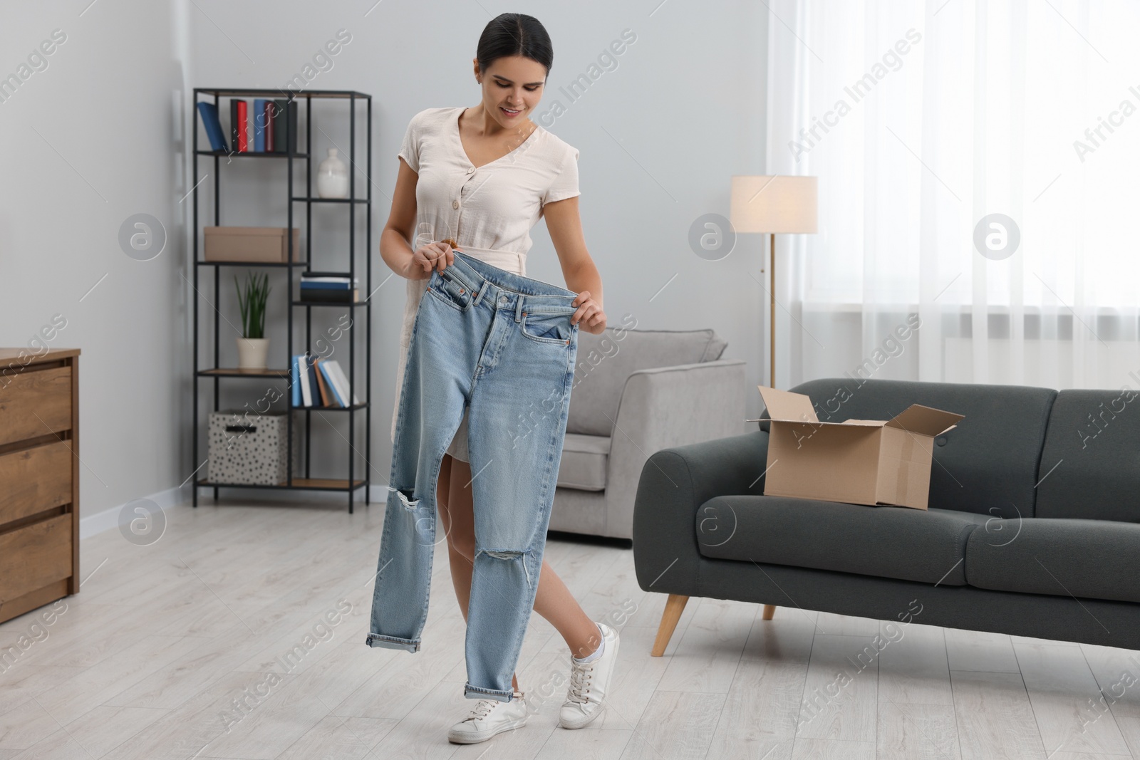 Photo of Young woman with just unpacked new jeans at home, space for text. Online shopping