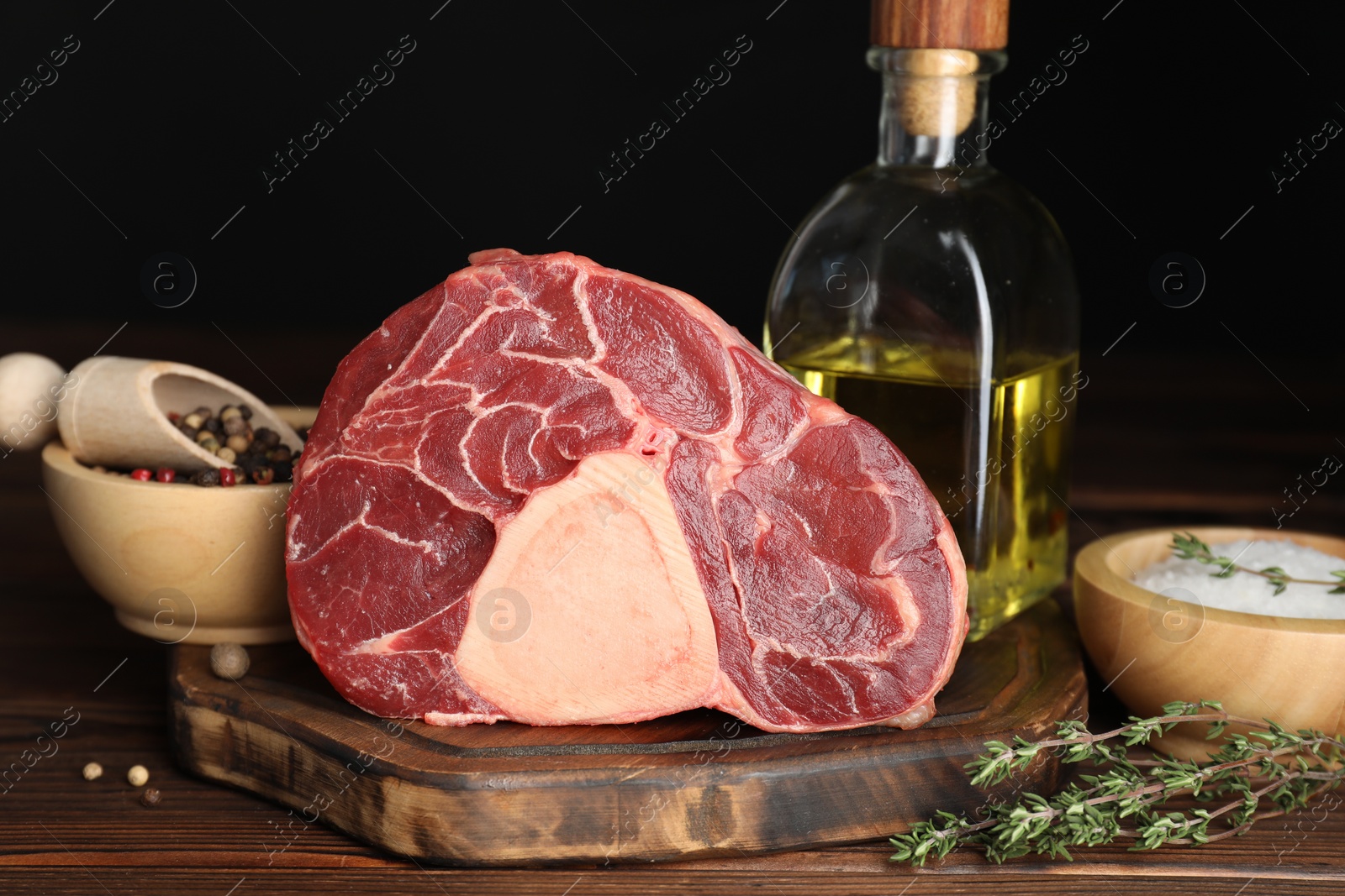 Photo of Piece of raw beef meat, thyme, oil and spices on wooden table against black background, closeup