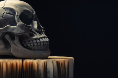 Photo of Human skull and old book on black background. Space for text