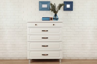 Photo of Modern chest of drawers with decor near white brick wall