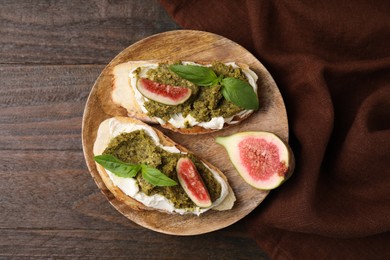 Photo of Tasty bruschettas with cream cheese, pesto sauce, figs and fresh basil on wooden table, top view