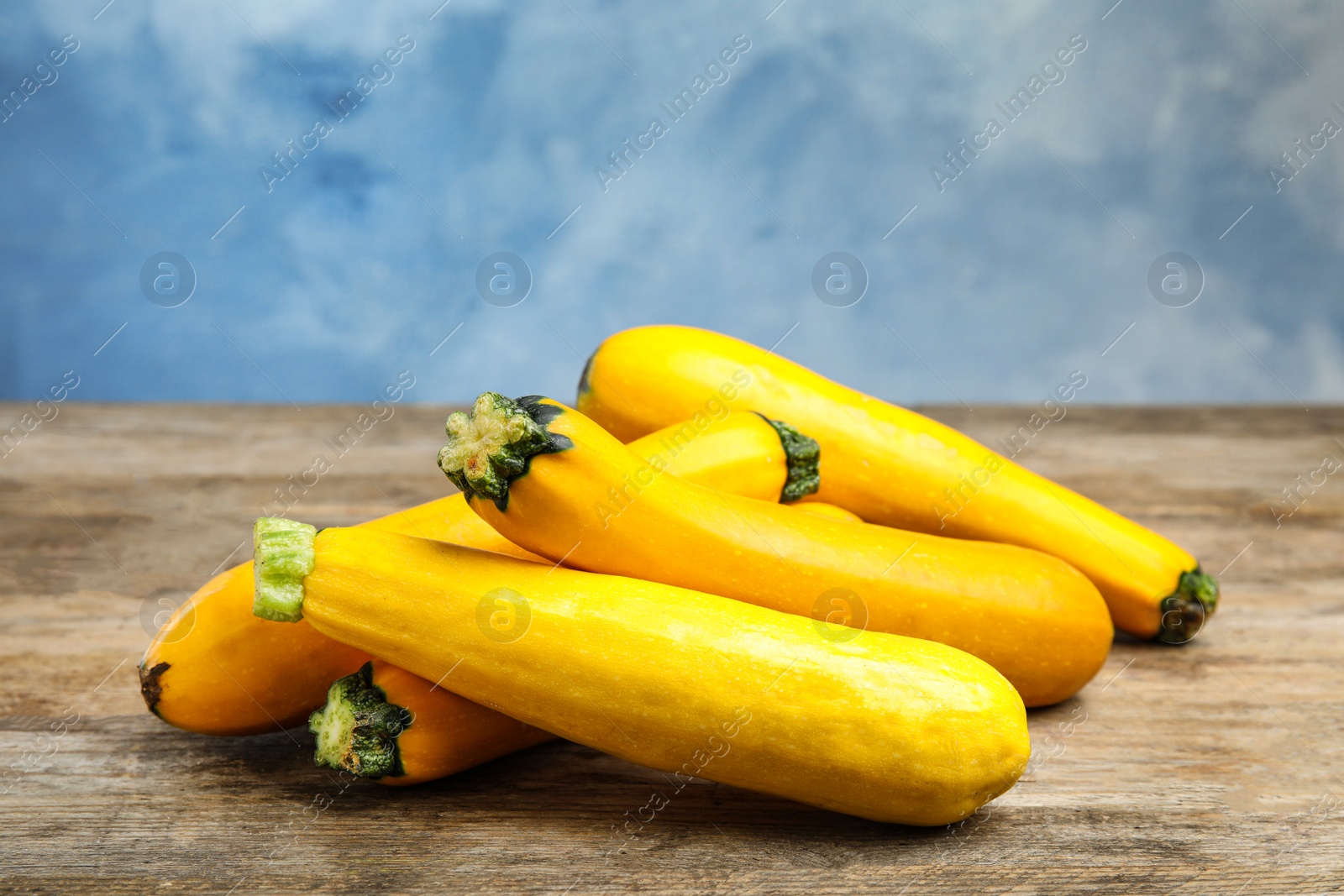 Photo of Fresh ripe yellow zucchini on wooden table against blue background