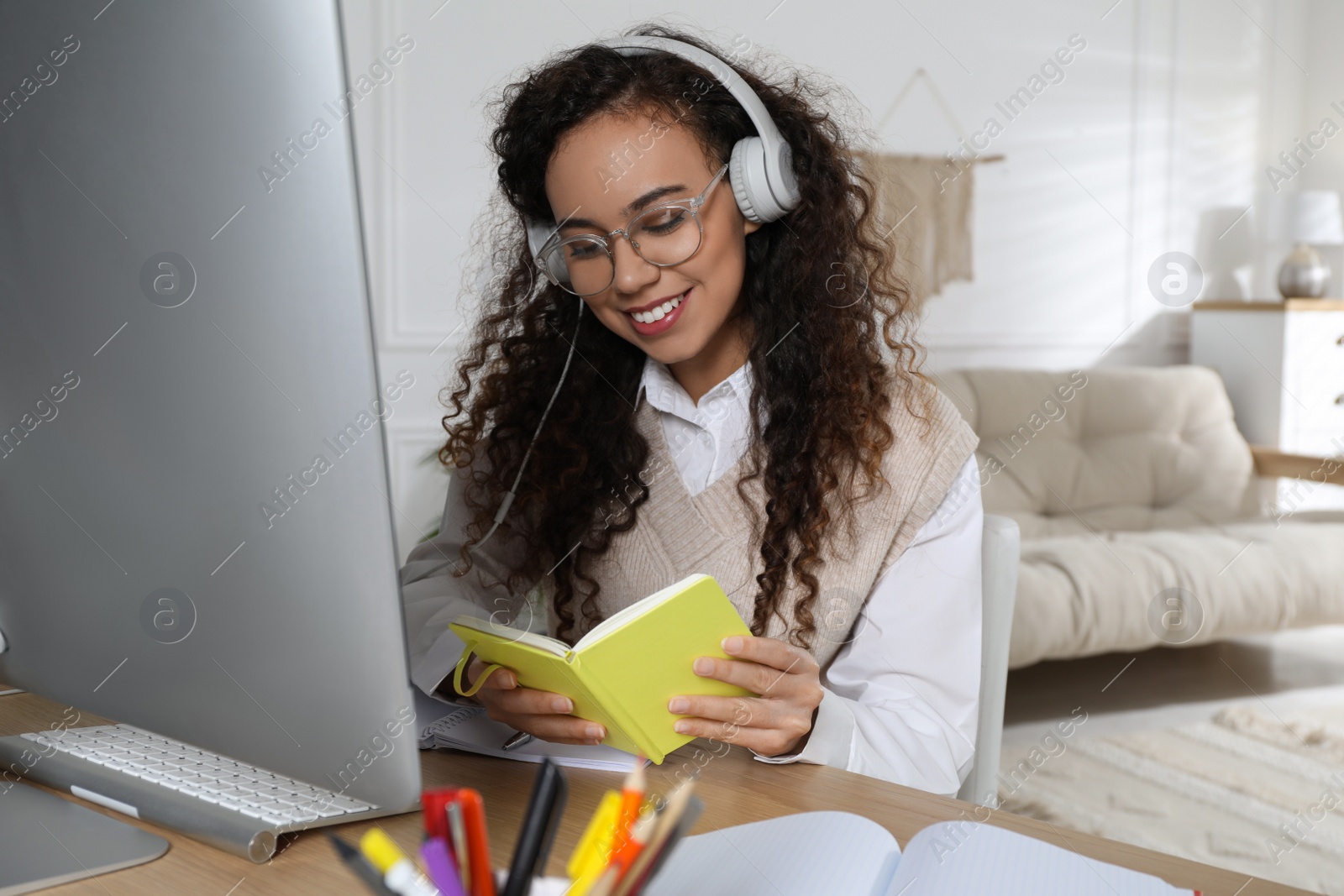 Photo of African American woman with headphones using modern computer for studying at home. Distance learning