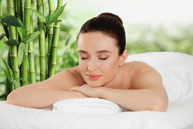 Beautiful young woman relaxing in spa salon. Green bamboo stems on background