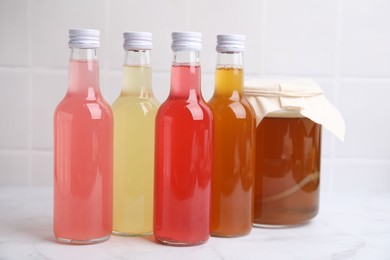 Photo of Delicious kombucha in glass bottles and jar on white marble table