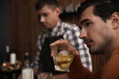 Photo of Young man with glass of whiskey in bar. Space for text