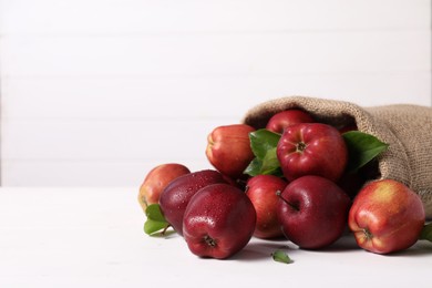 Photo of Ripe red apples and green leaves on white table. Space for text