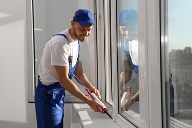Photo of Worker sealing plastic window with caulk indoors. Installation process